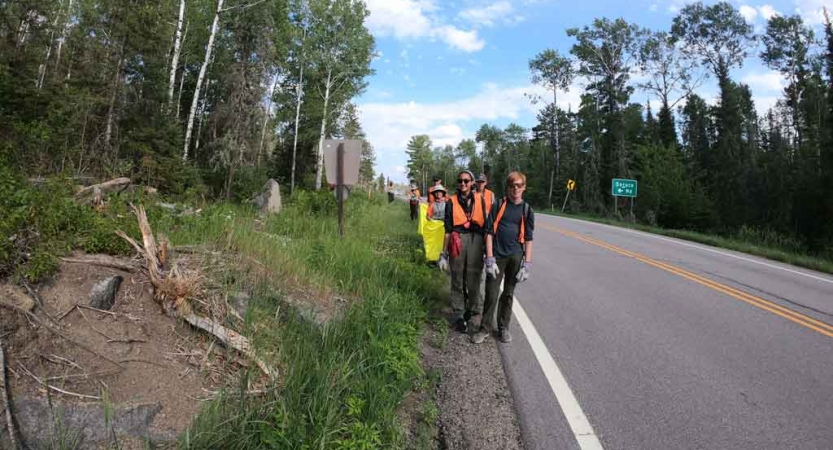a group of students wearing brightly colored vests participate in a service project beside a road